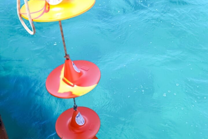 Boyas luminosas rojas y amarillas flotando sobre el agua turquesa junto al casco