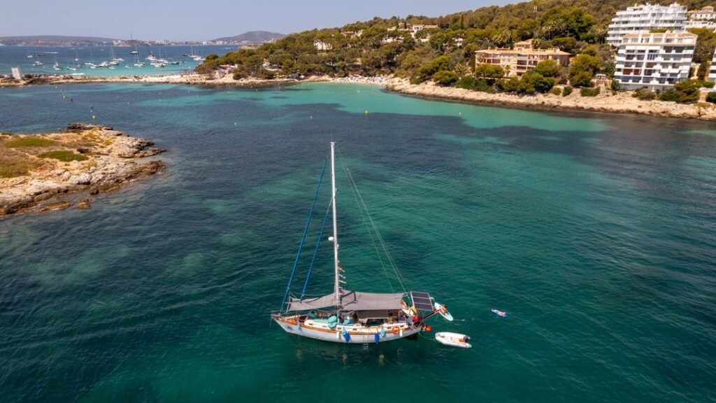 Vista aérea de un velero fondeado en una cala de aguas turquesa