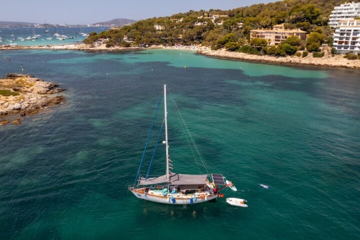 Vista aérea de un velero fondeado en una cala de aguas turquesa