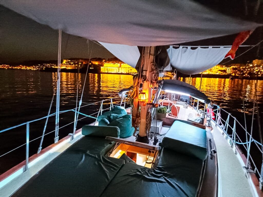 Cubierta de un velero de noche, con las luces de una ciudad al fondo