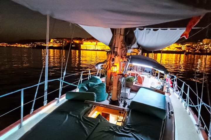 Cubierta de un velero de noche, con las luces de una ciudad al fondo
