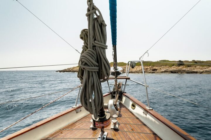 Proa de un velero con un cabo enrollado y la costa al fondo