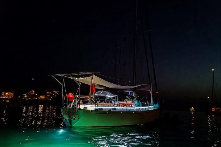 Velero fondeado de noche, con luces verdes bajo el agua