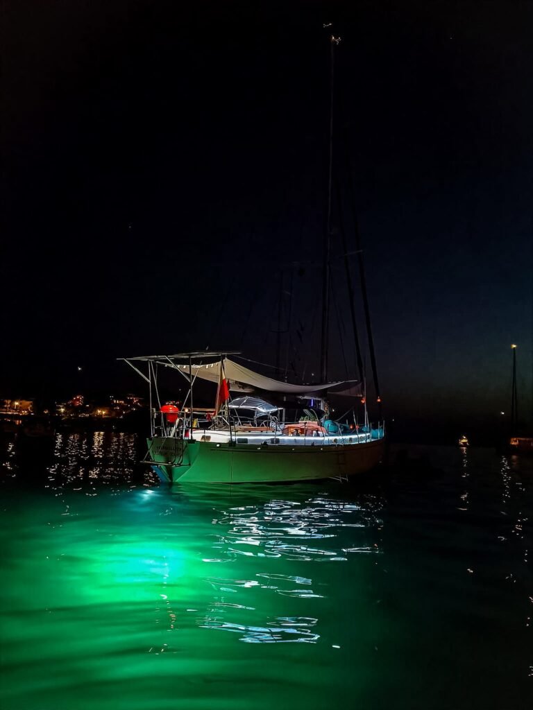 Velero fondeado de noche, con luces verdes bajo el agua